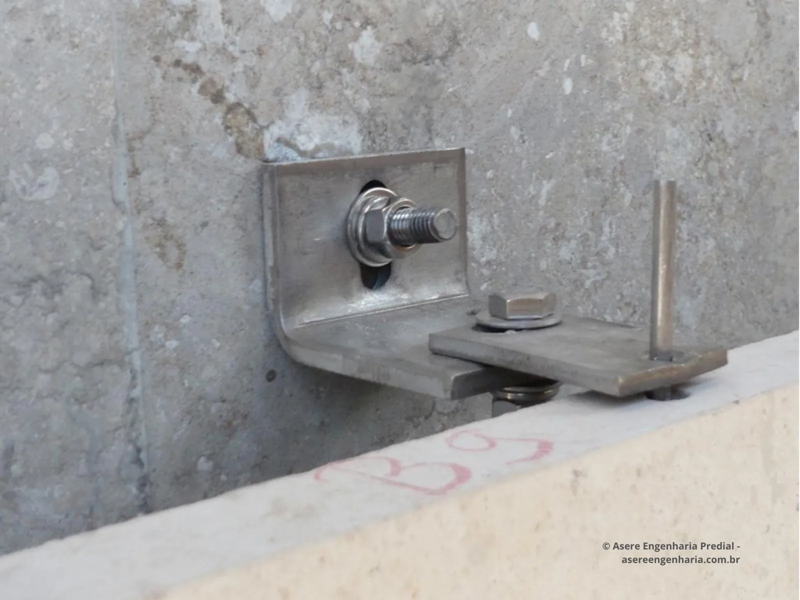 Detalhe aproximado de inserto metálico em L com parafuso de fixação e pino para encaixe da placa.