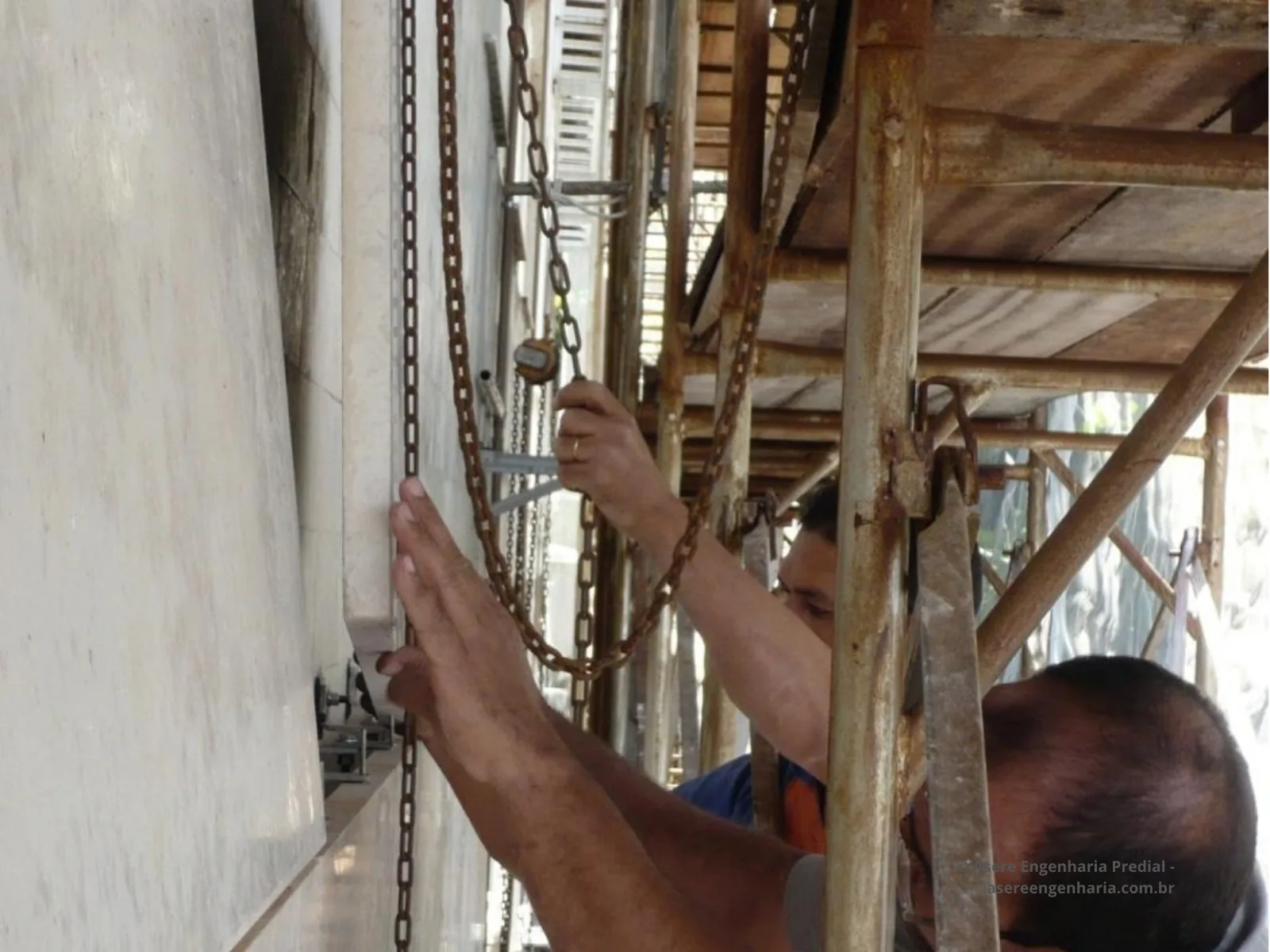 Montadores instalando placas de pedra na fachada durante a obra de retrofit, com andaime.